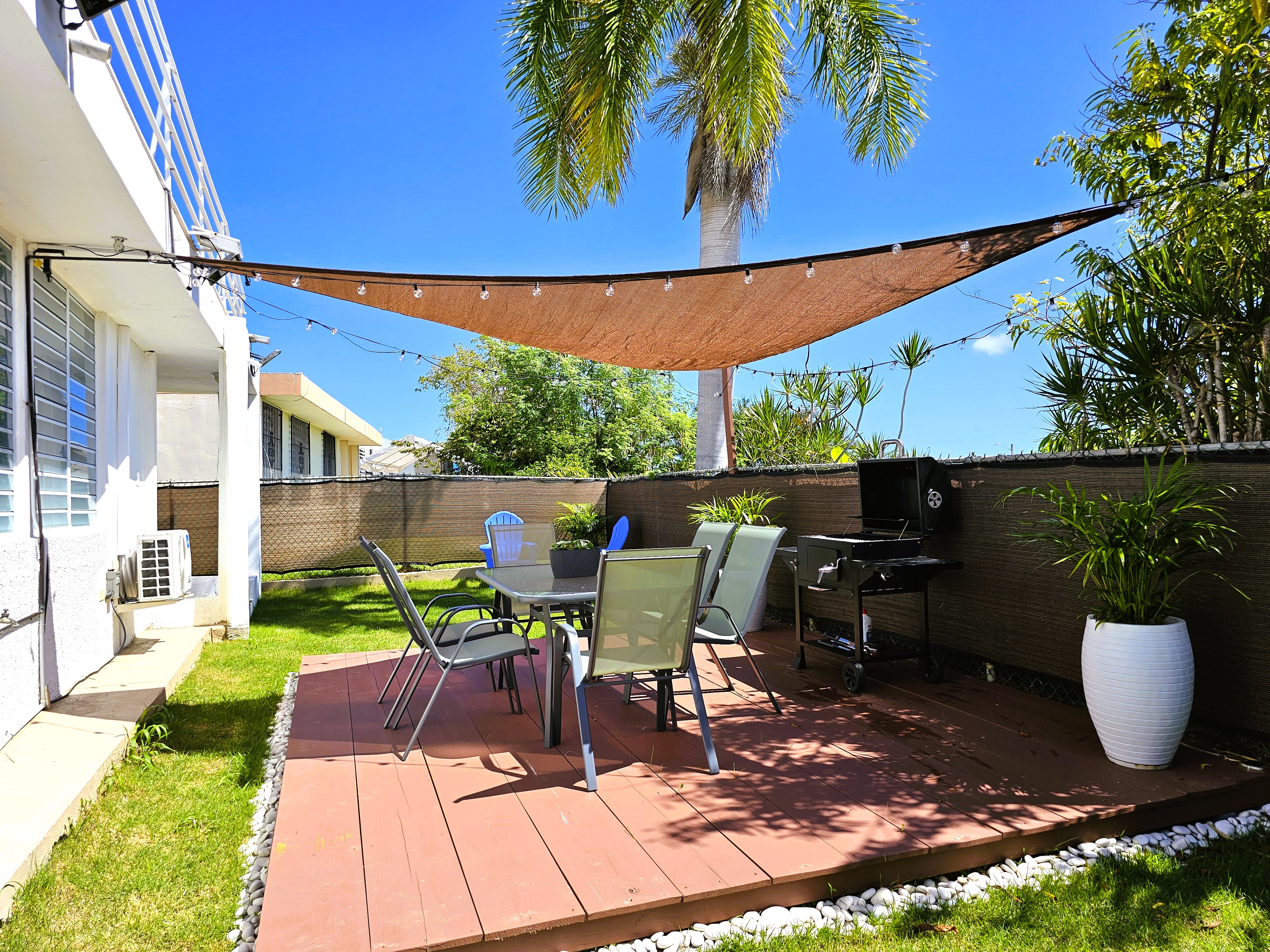 Private tropical patio with shaded dining deck, BBQ, and palm-lined yard