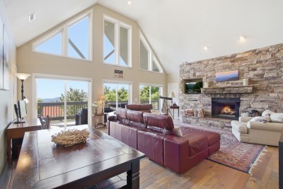 Vaulted great room with stone fireplace, wall of windows, and view deck