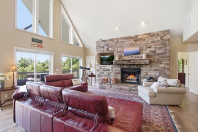 Bright vaulted living room with stone fireplace, deck access, and scenic views