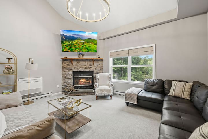 Bright living room with stone fireplace, large windows, and cozy seating