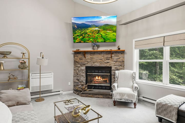 Cozy living room with stone fireplace, big windows, and wooded views