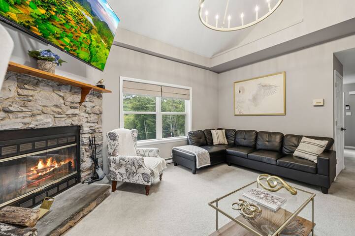 Cozy vaulted living room with stone fireplace and serene wooded views