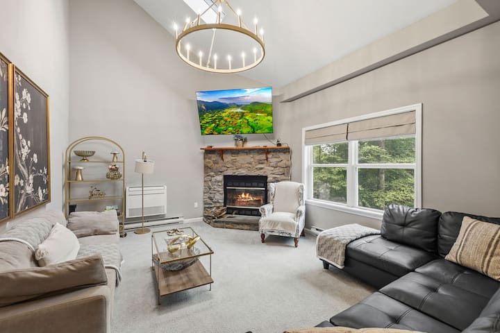 Bright vaulted living room with stone fireplace, big windows, and cozy seating