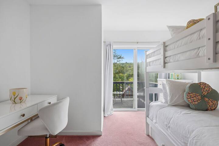 Bright bunk room with desk, balcony access, and peaceful treetop views