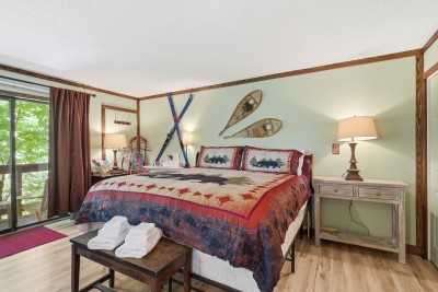 Cozy lodge-style bedroom with king bed, rustic decor, and treetop views