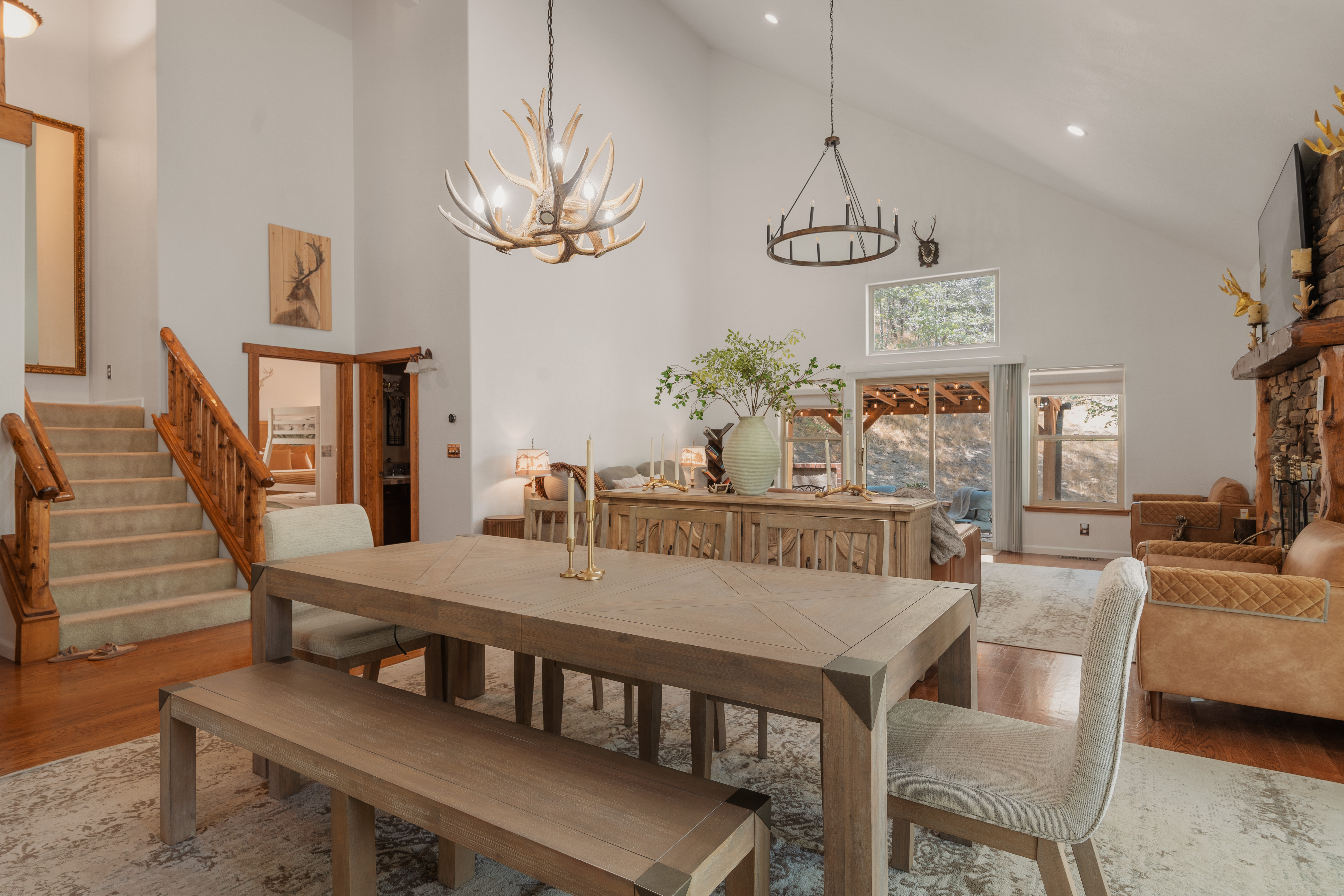 Vaulted rustic great room with fireplace, woodland views, and elegant dining
