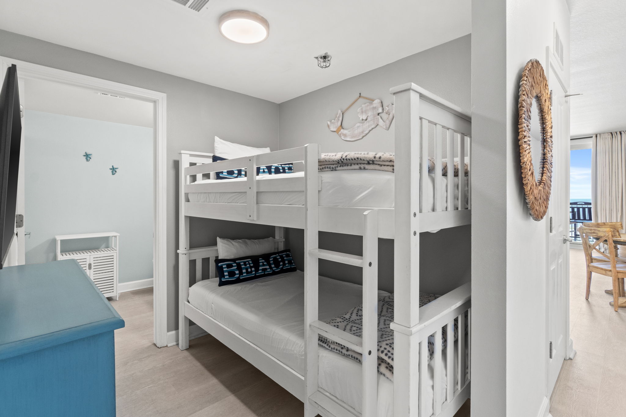 Coastal bunk room with bright white beds and balcony access
