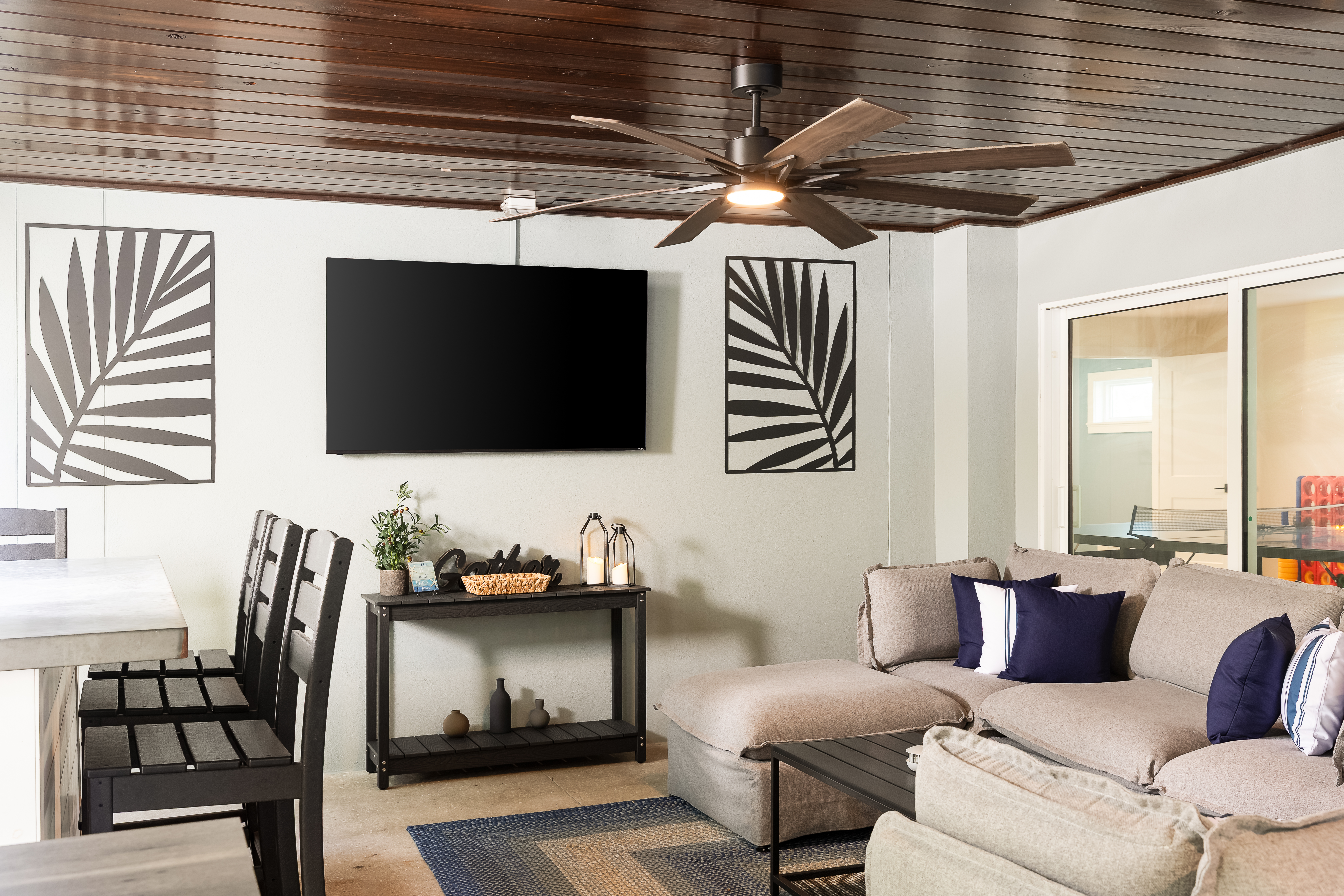 Covered lounge with large sectional, dining space and wall-mounted TV