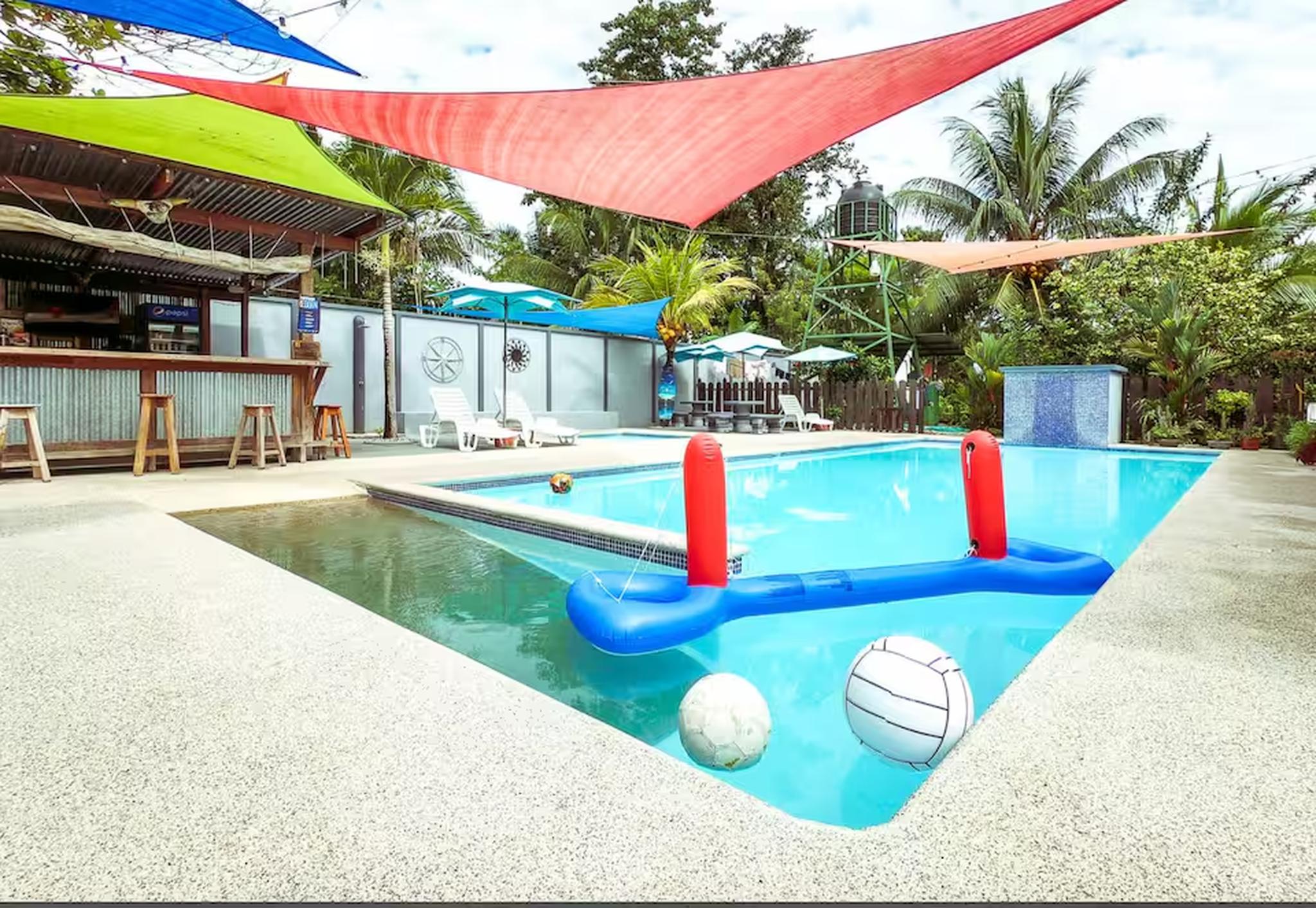Tropical resort-style pool with shade sails, water feature, and open-air bar