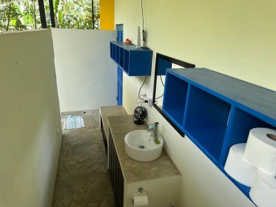 Bright semi-open bathroom with modern sink, bold shelving, and tropical light