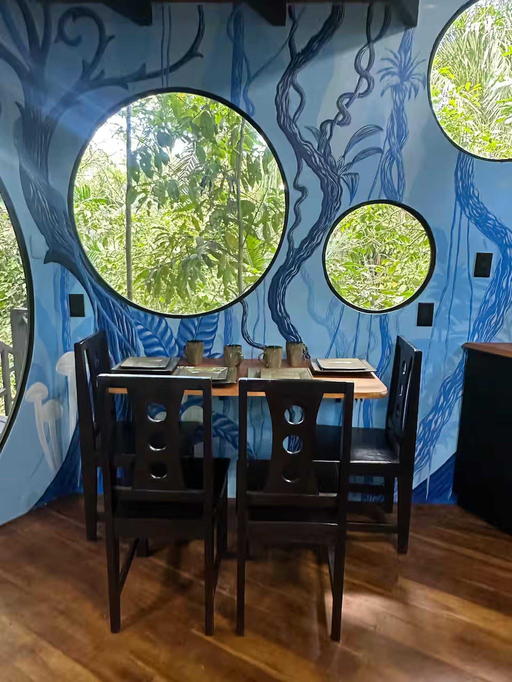 Artistic dining nook with jungle mural and round windows to tropical views