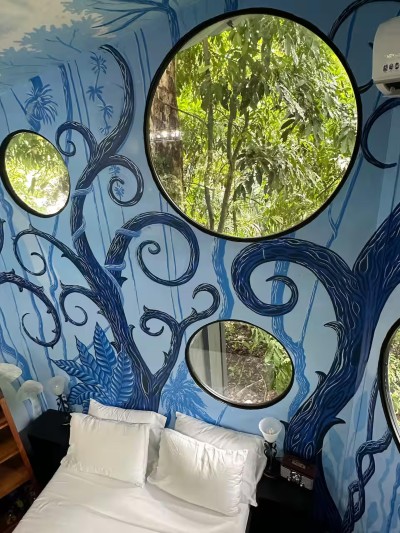 Artful jungle-themed bedroom with round windows and lush forest views