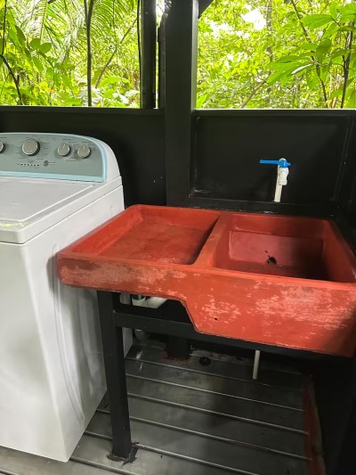 Open-air laundry area with rustic sink and lush tropical views