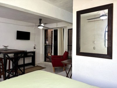 Bright studio with TV, dining nook, red lounge chair, and balcony access