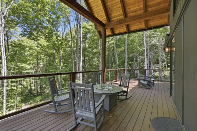 Private covered deck featuring forest views, dining space, and rocking chairs — a charming spot to relax, share meals, and soak in the peaceful sounds of the surrounding woods.
