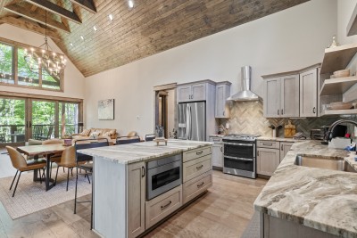 Spacious vaulted great room featuring a chef’s kitchen and stunning forest views — a warm, airy space perfect for cooking, gathering, and relaxing together throughout your stay.