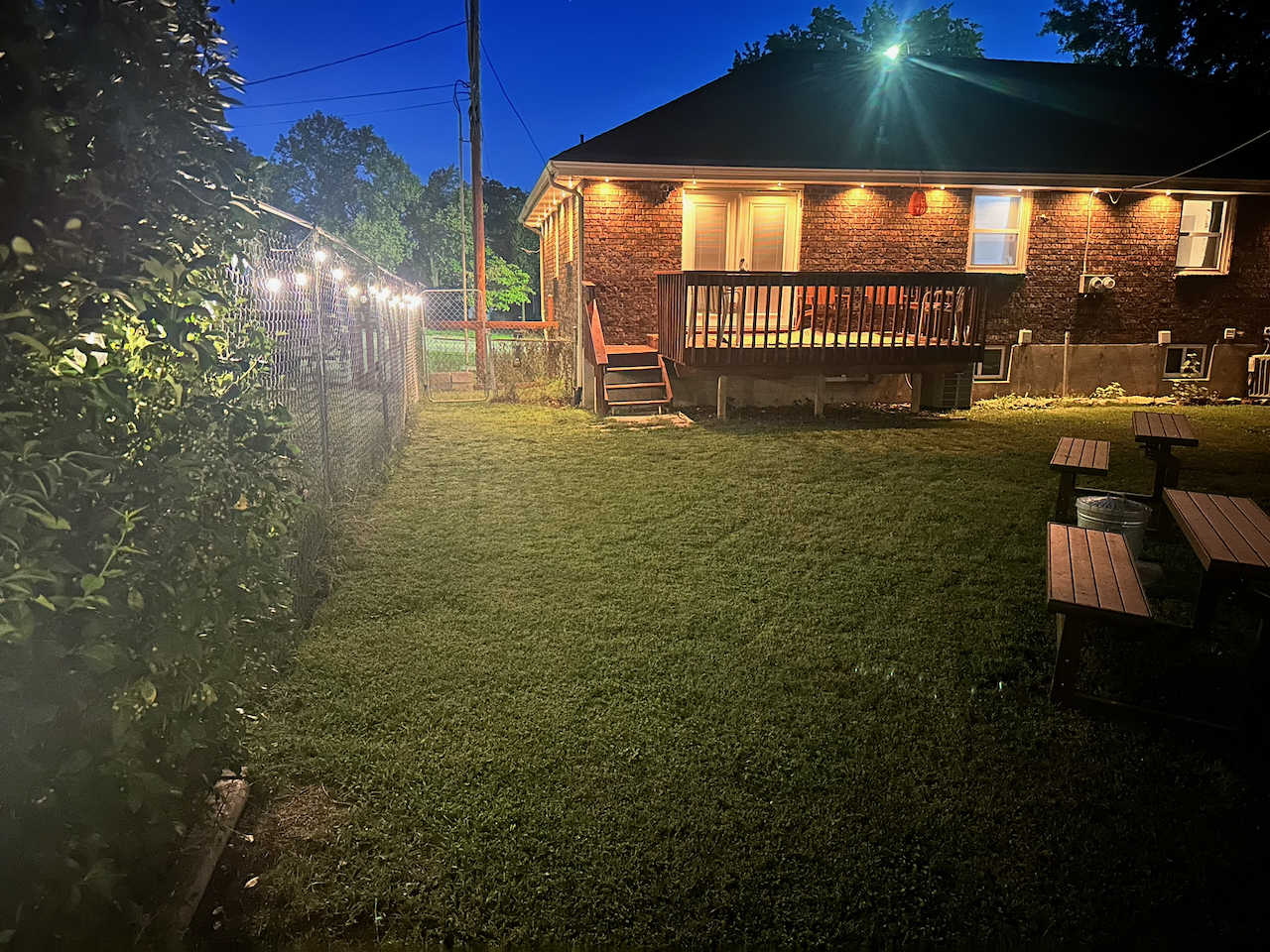 Cozy fenced backyard with deck, lawn, and glowing string lights