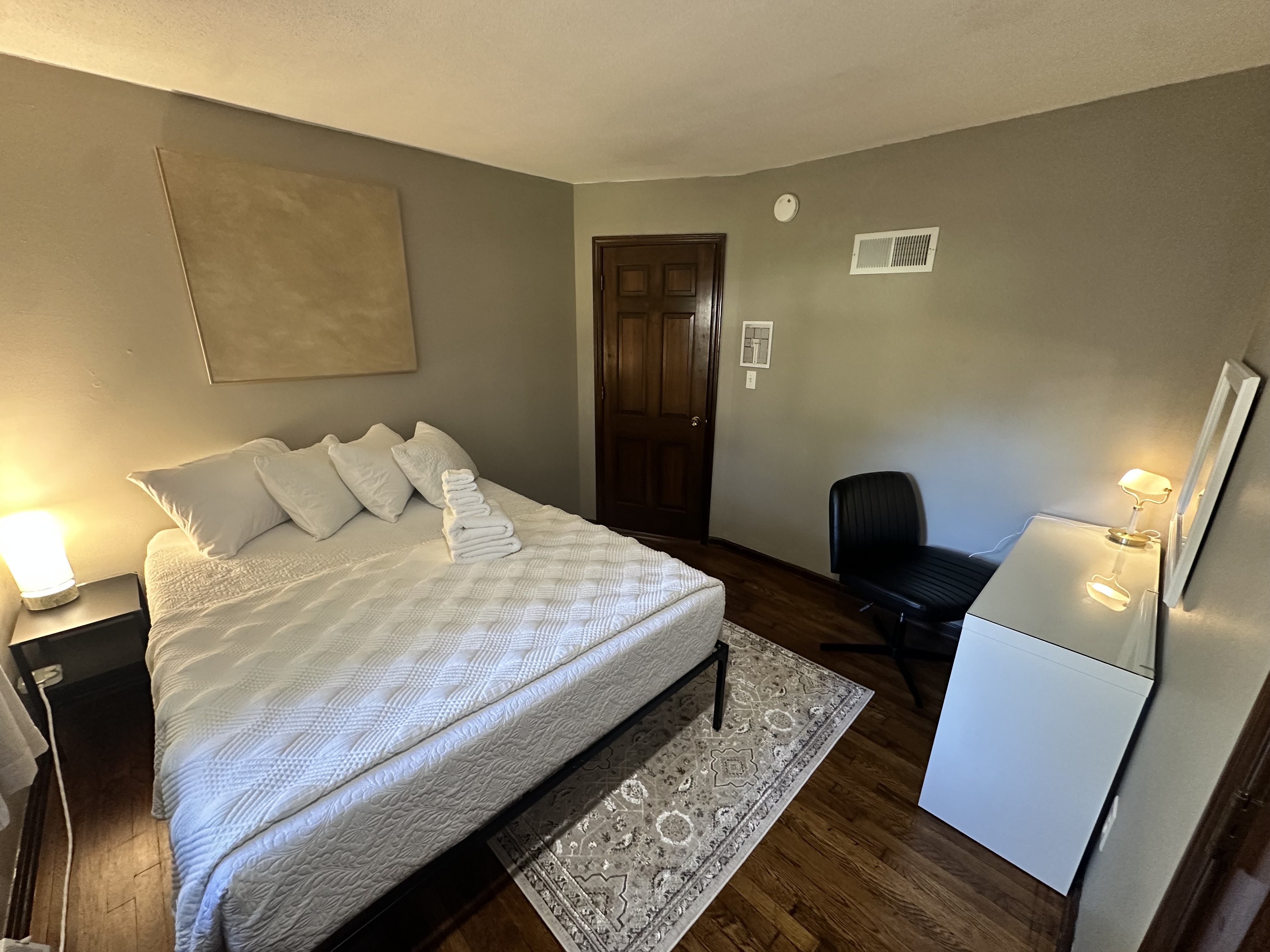 Cozy queen bedroom with warm lighting, wood floors, and guest-ready touches
