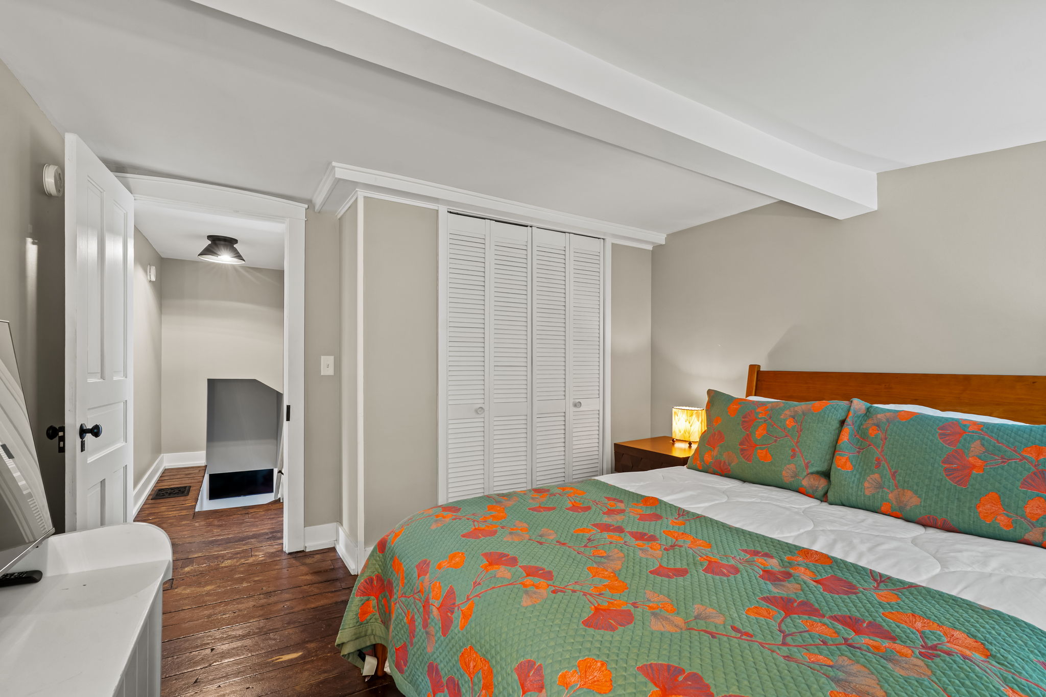 Cozy bedroom with hardwood floors, bright linens, and built-in closet