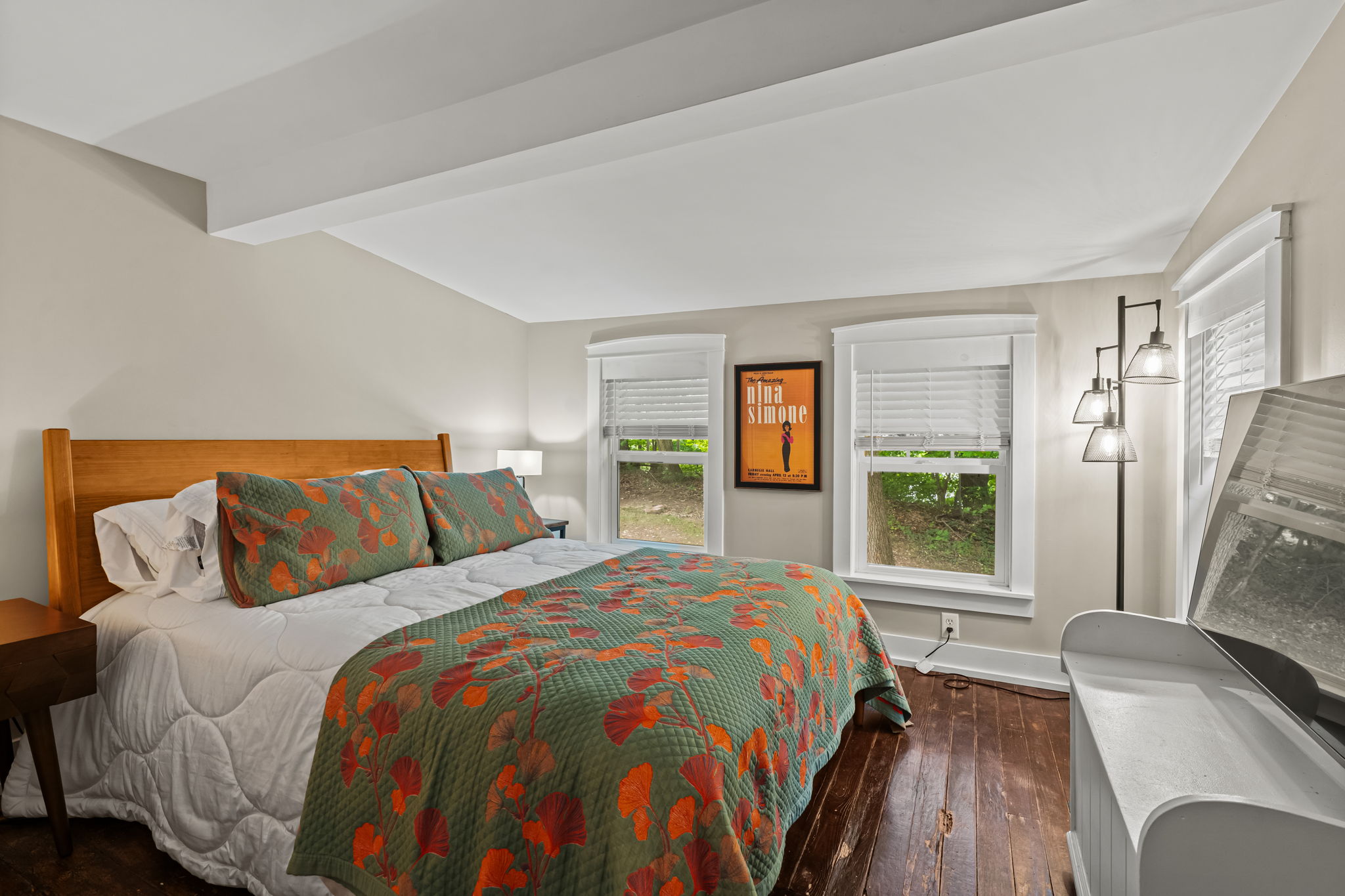 Bright, cozy bedroom with hardwood floors, TV, and cheerful floral bedding