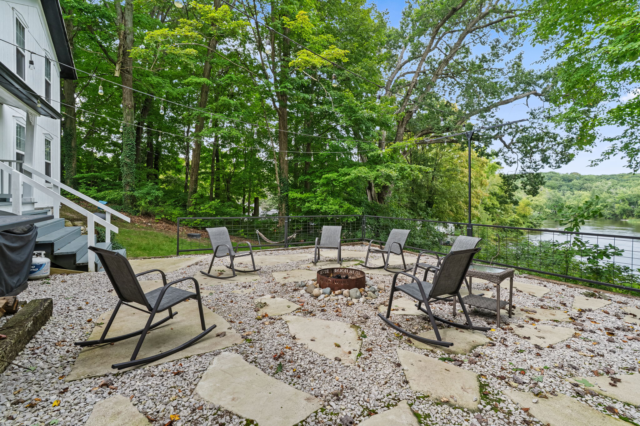 Fire pit patio with rocking chairs, string lights, and peaceful water views