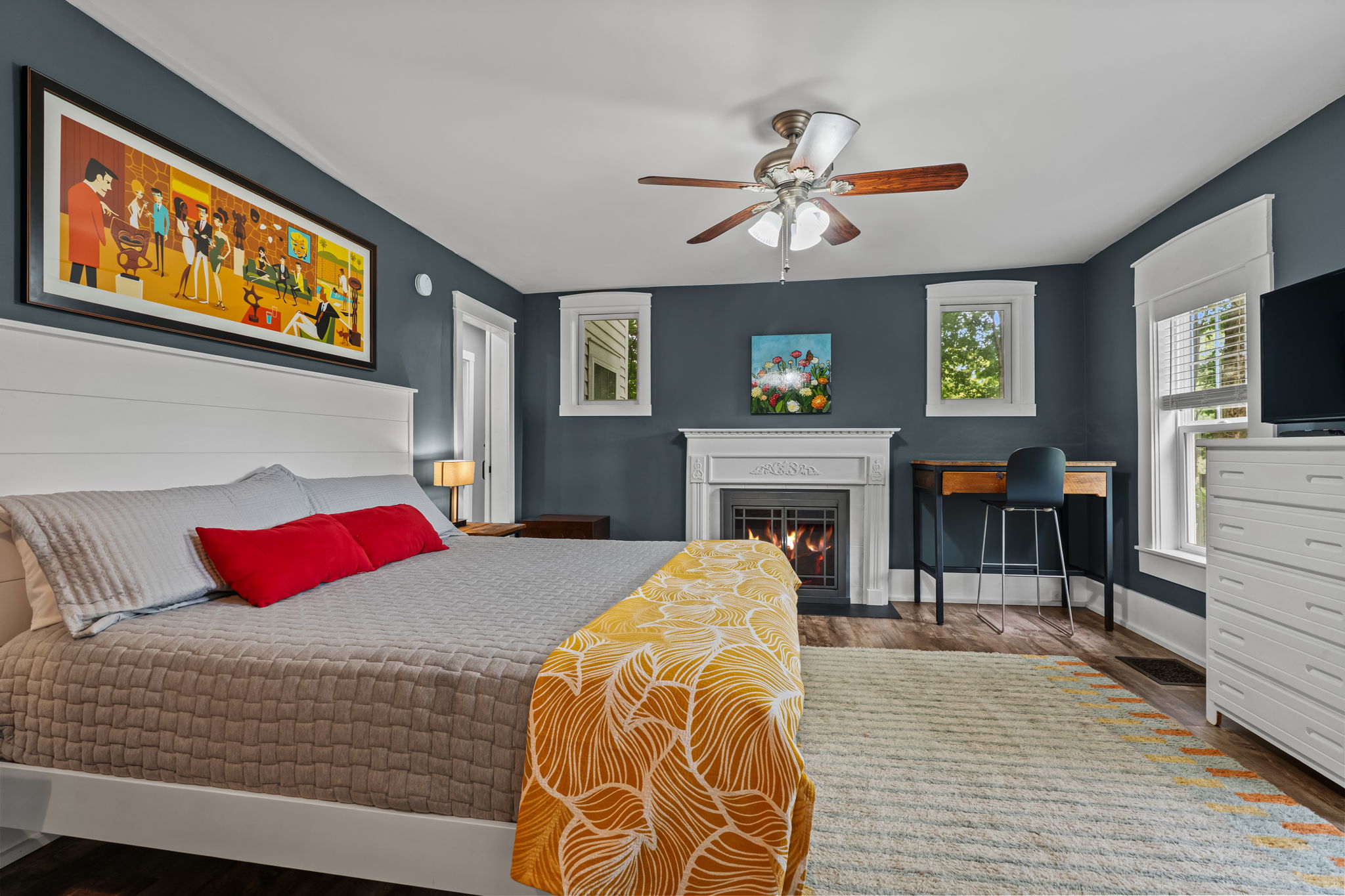 Cozy, art-filled bedroom with fireplace, desk, and bright natural light