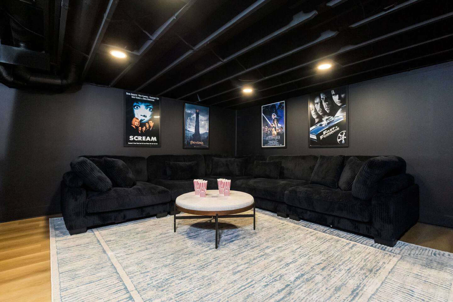 Dark screening room with a black corduroy sectional and framed movie posters
