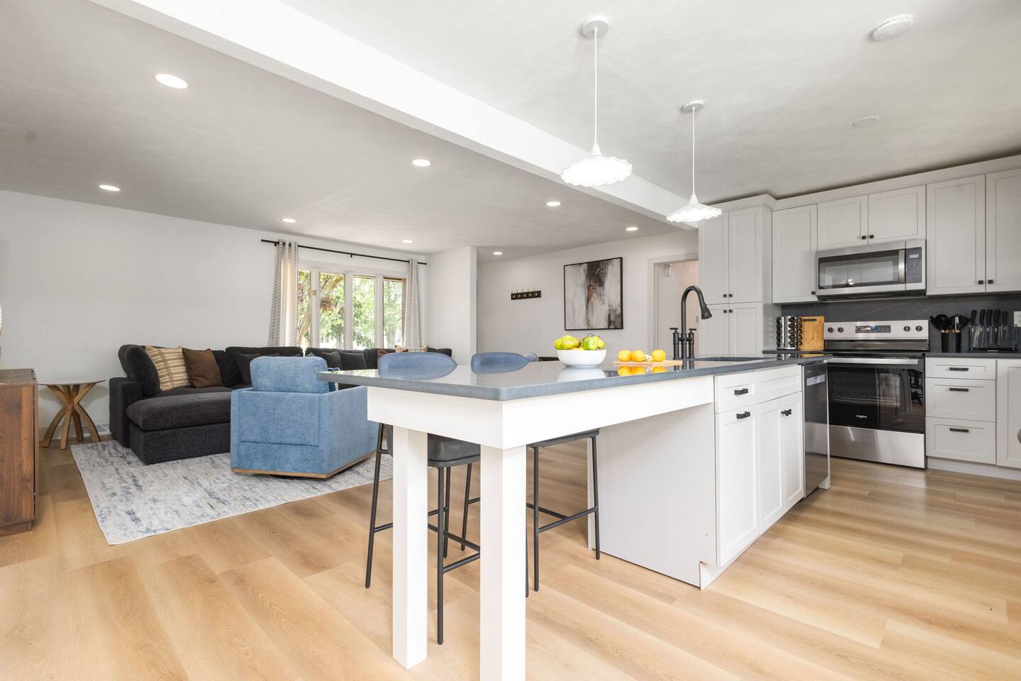 White kitchen with a long island, stainless appliances and pendant lights