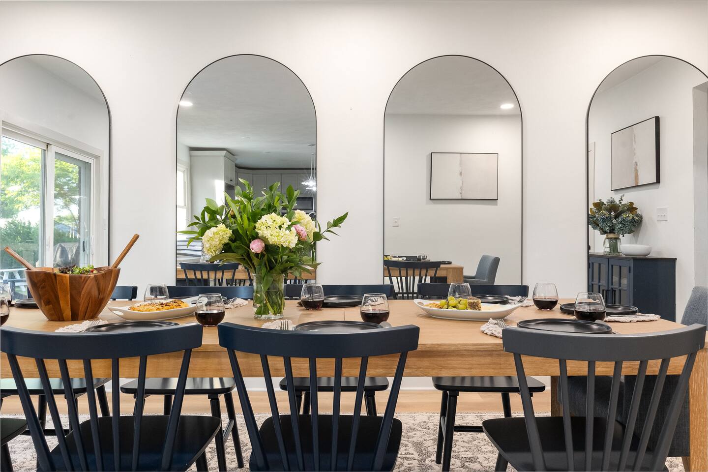 Dining table set with place settings and flowers in front of tall arched mirrors