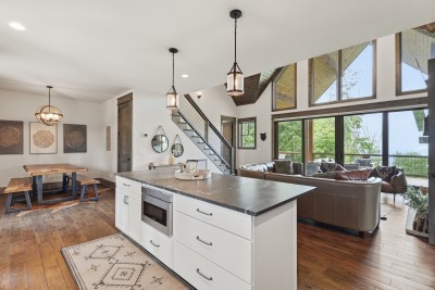 Sleek waterfall-edge island anchors the open kitchen, flowing into the vaulted living area with soaring windows, exposed wood ceilings, and a striking staircase — the heart of the home for cooking, gathering, and making memories.