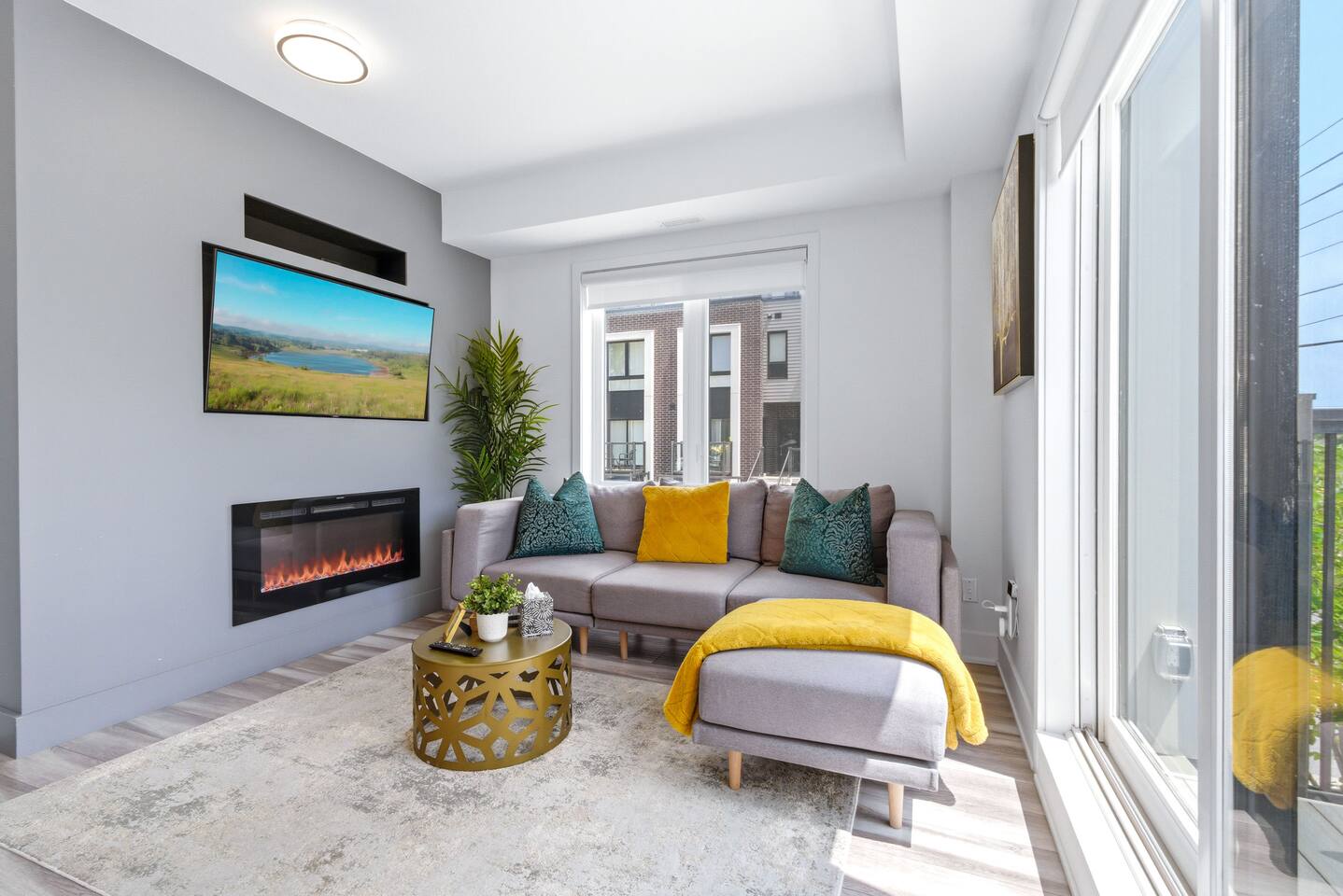 Bright living room with cozy seating, balcony light, mounted TV, and fireplace, creating a warm space to relax and unwind.