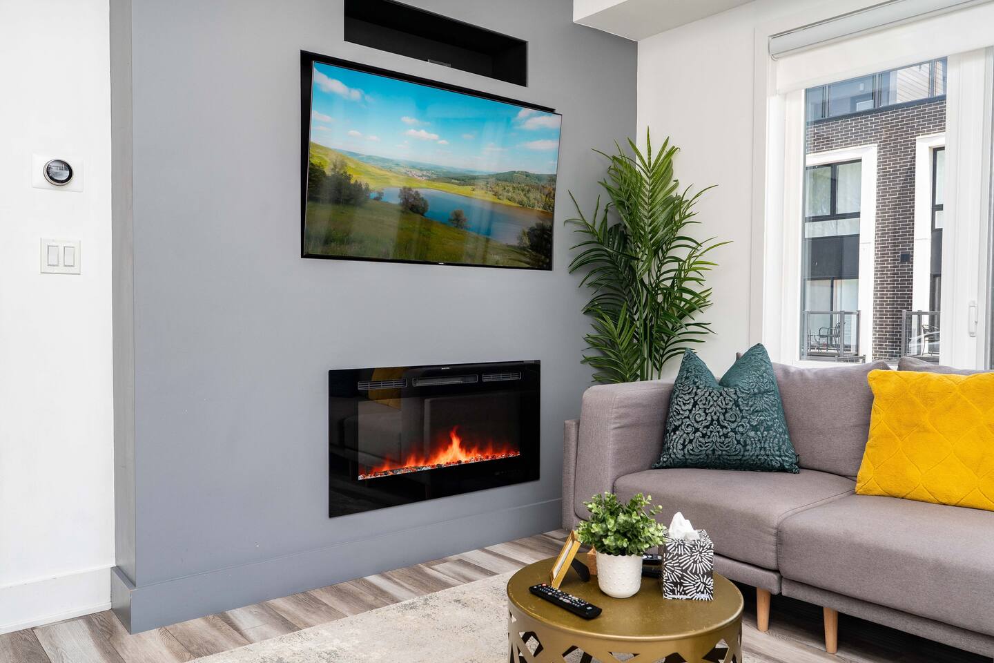 Cozy living room with a mounted TV, electric fireplace, soft seating, and greenery, creating a warm space to relax indoors.