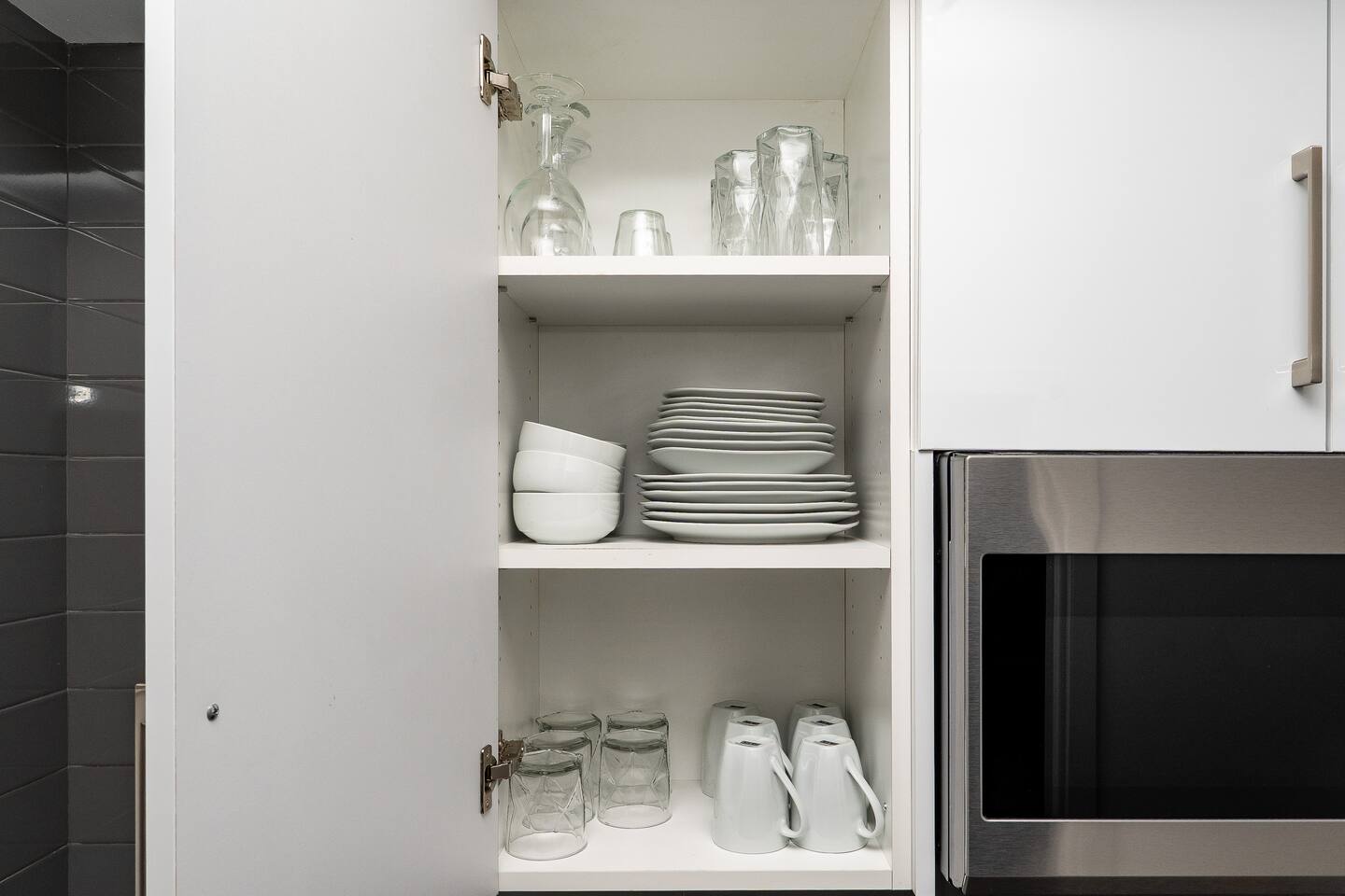 Open cabinet with neatly arranged dishes, glasses, and mugs, giving guests easy access to kitchen essentials during their stay.