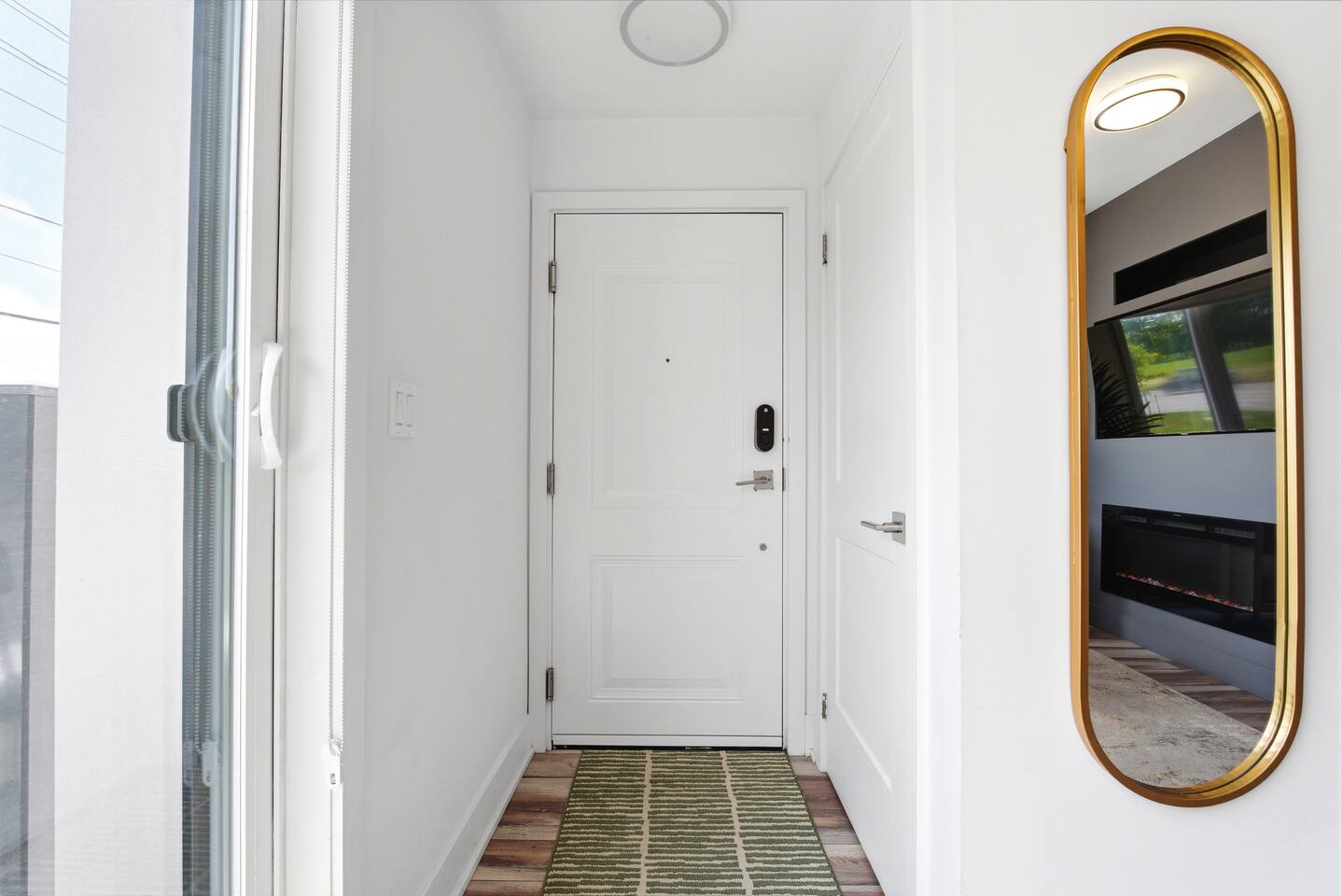 Bright entryway with a clean door area, mirror, and runner rug, offering a simple and welcoming arrival space.