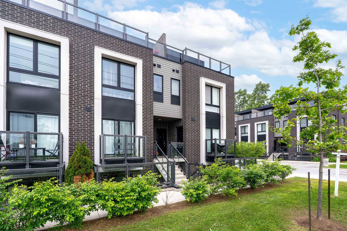 Modern townhouse exterior with landscaped greenery, private balconies, and a clear entry path, offering a polished and welcoming arrival.