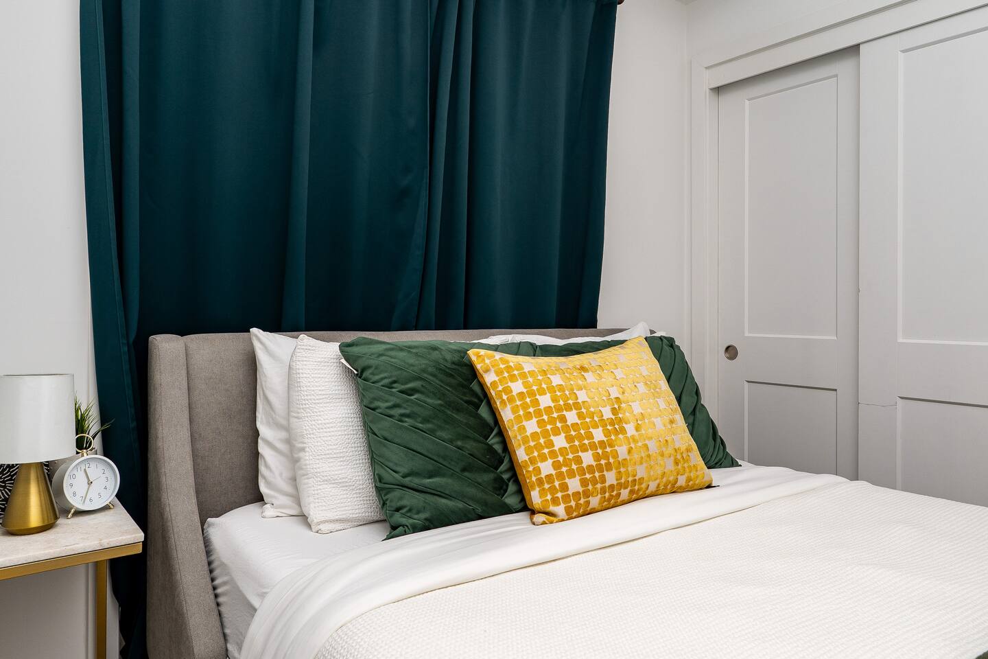 Comfortable bed with layered pillows and dark curtains, creating a cozy space for restful sleep.