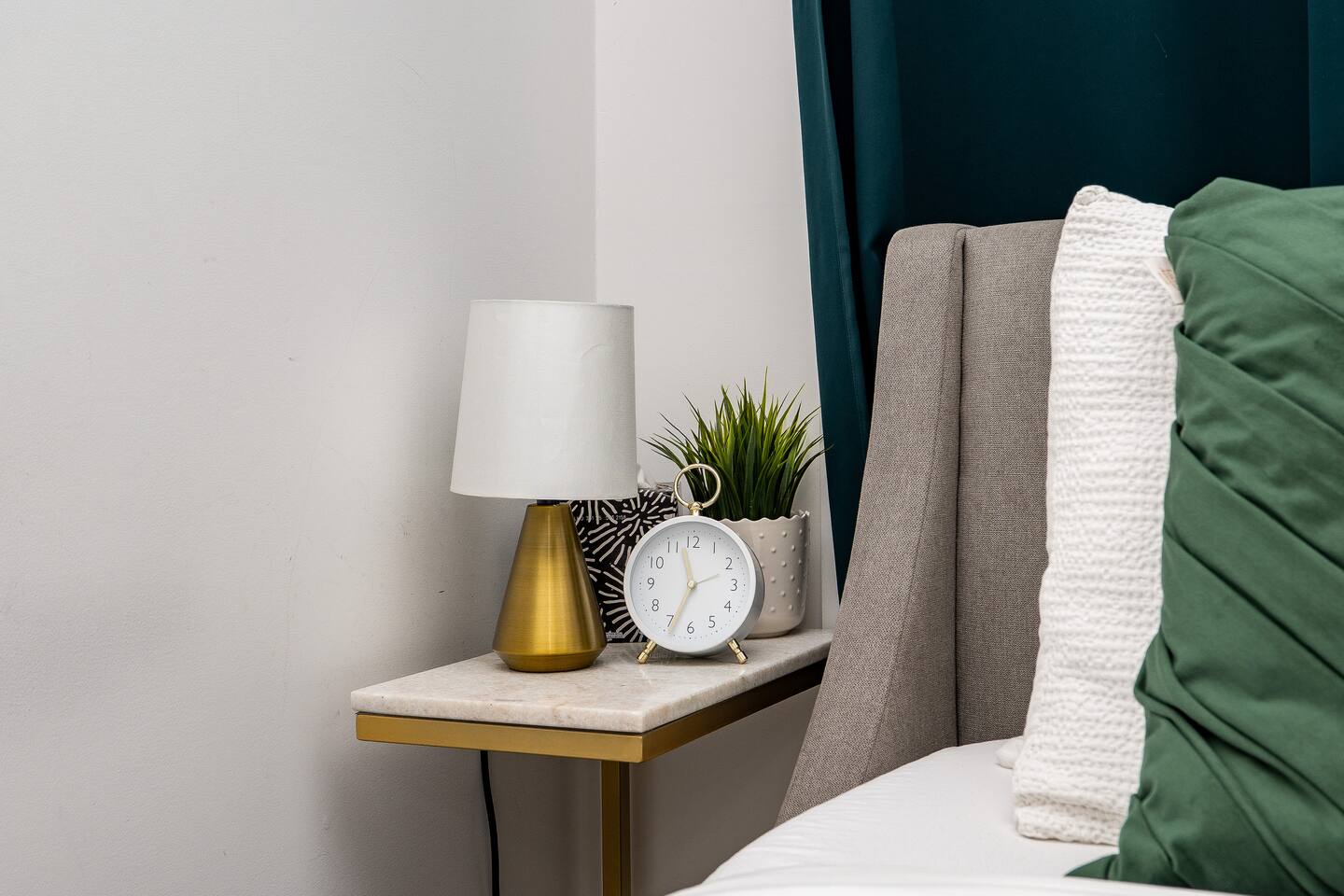 Bedside table with warm lighting, simple decor, and fresh accents, adding comfort and convenience beside the bed.