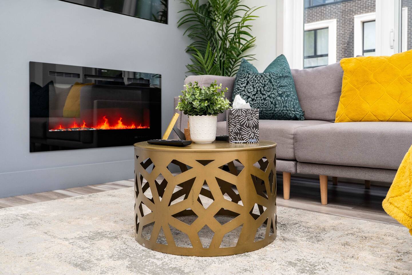 Stylish living room detail with a decorative coffee table, soft seating, greenery, and a nearby fireplace for a cozy indoor setting.