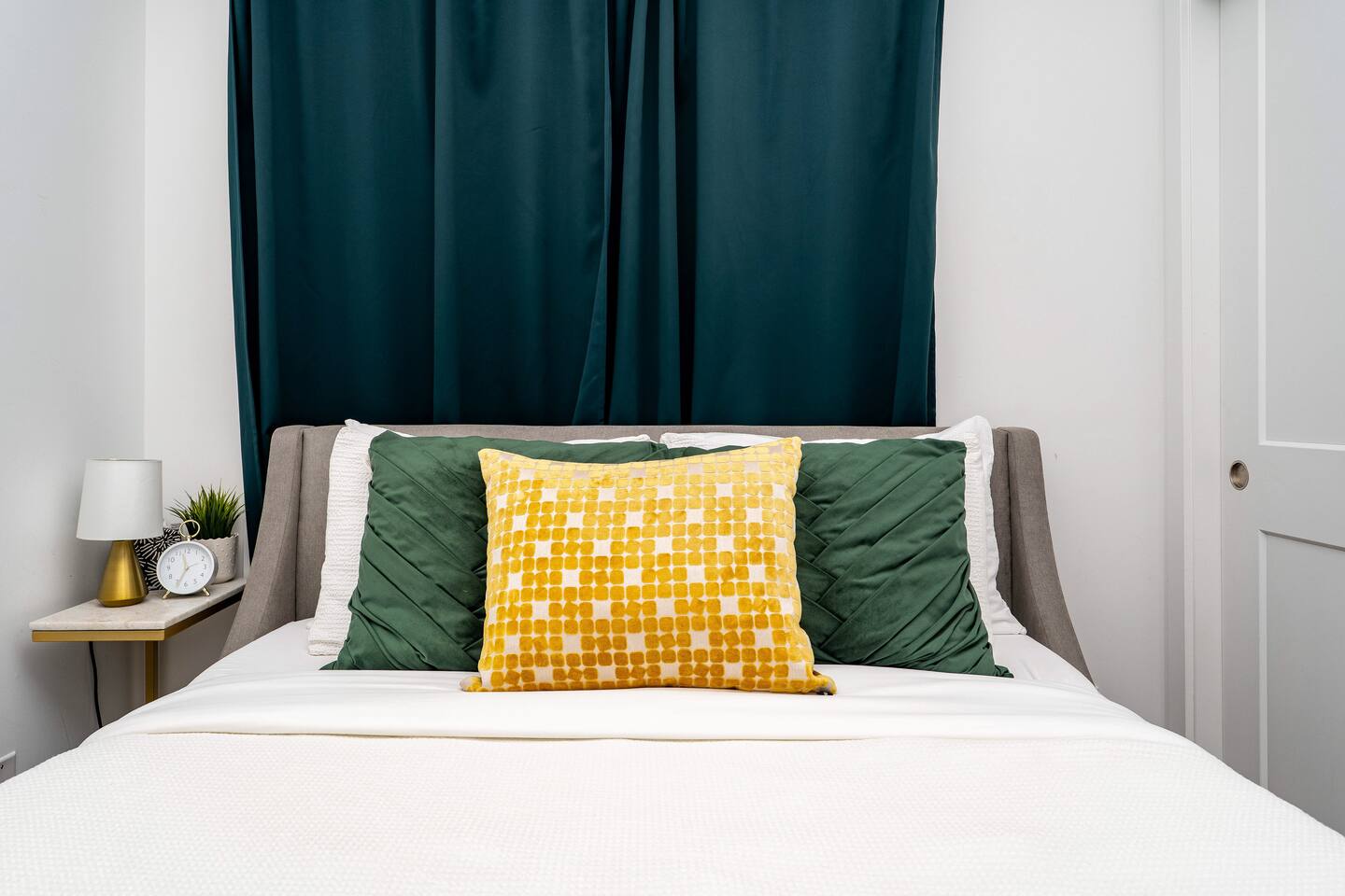 Bright bedroom detail with layered pillows, soft bedding, and rich curtain tones, creating a comfortable space to rest.