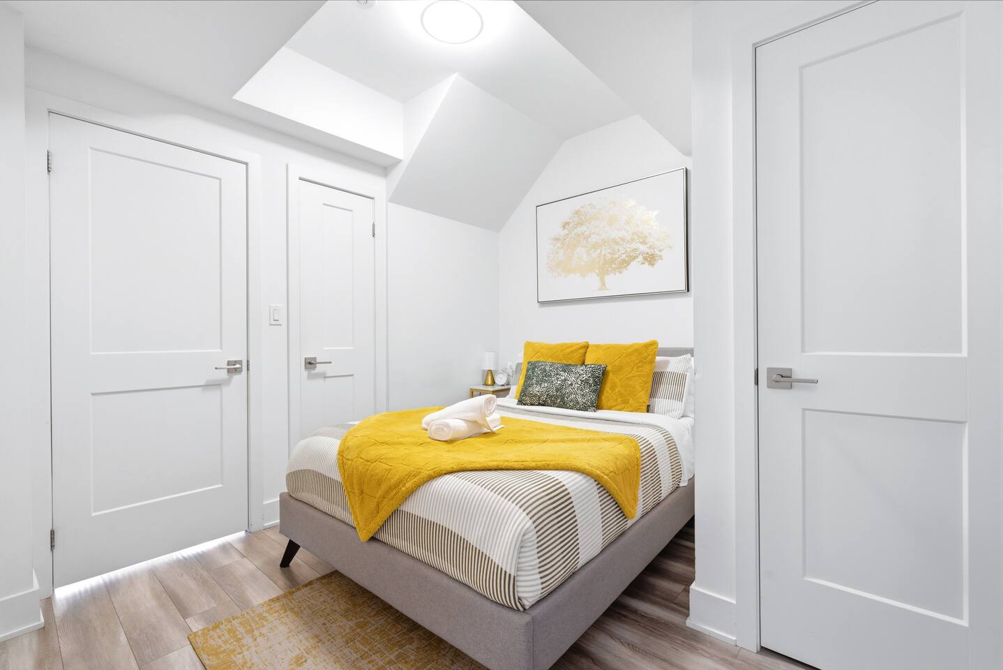 Cozy bedroom with warm yellow accents, fresh towels, soft bedding, and natural light, offering a comfortable space to rest.