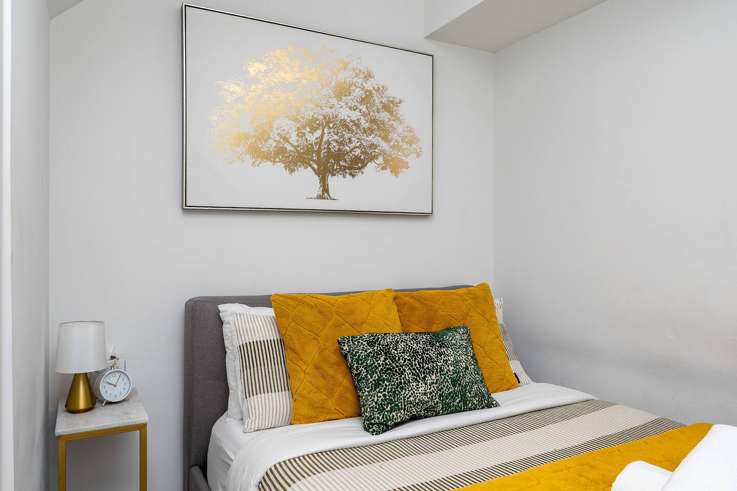 Cozy bedroom with layered pillows, warm yellow accents, and wall art, creating a calm and comfortable place to rest.