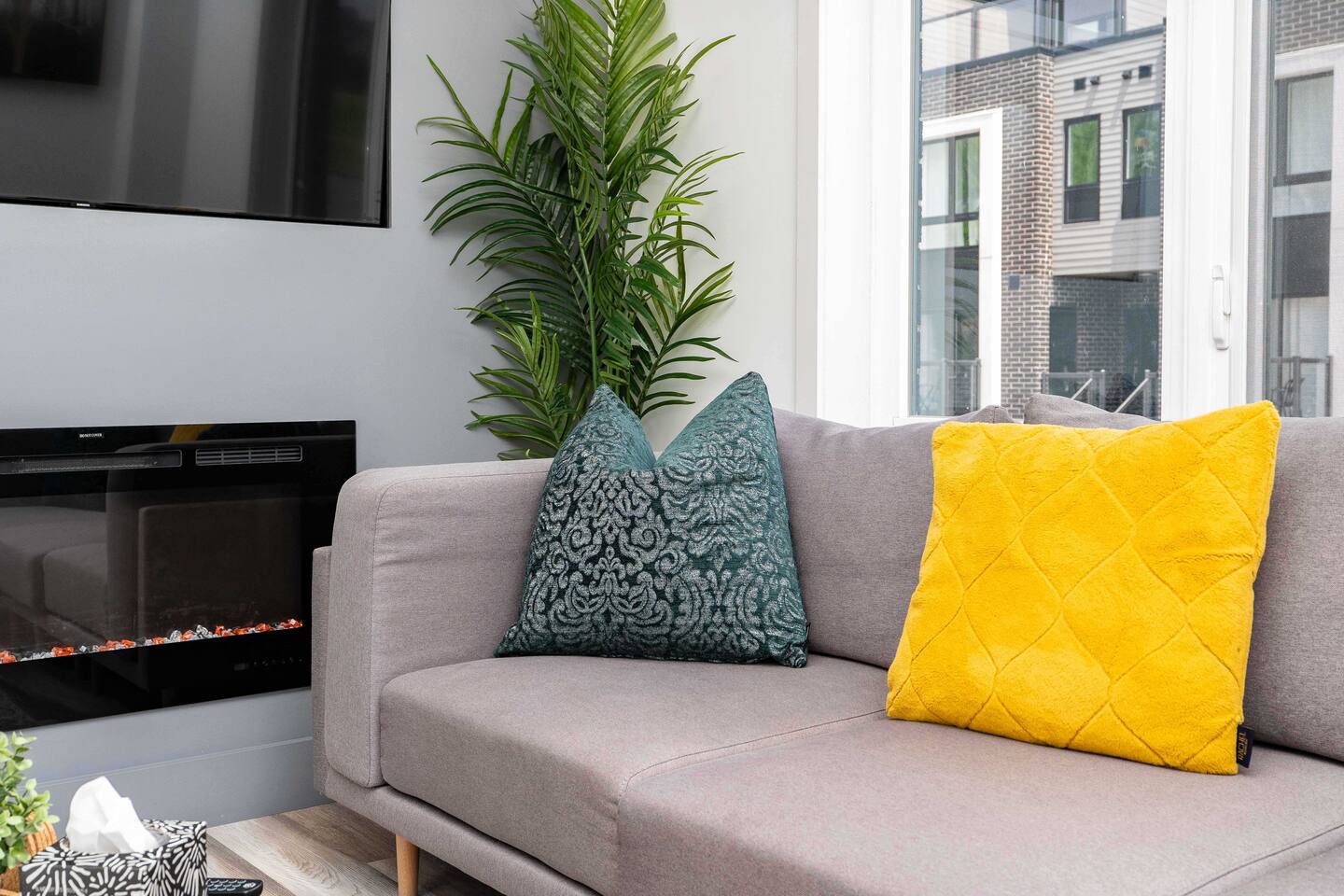Cozy living area with a soft sofa, leafy accent, and nearby fireplace, creating a warm spot to relax by the window.