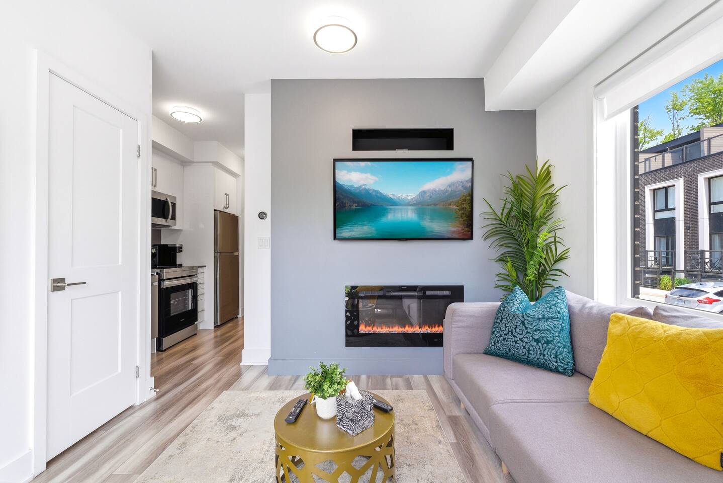 Bright living area with a mounted TV, electric fireplace, cozy seating, and kitchen nearby for a comfortable stay.