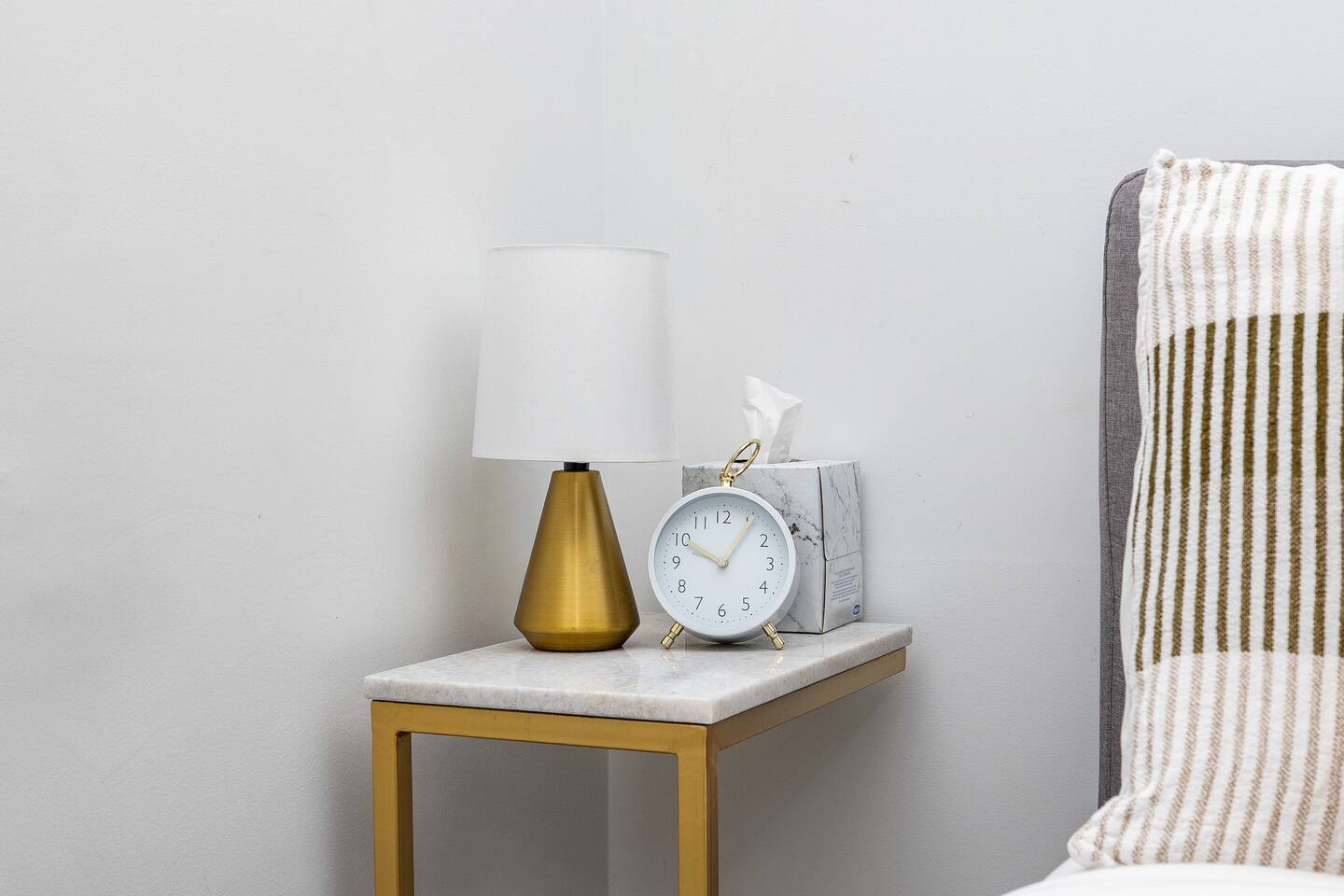 Bedside table with a lamp, clock, and tissues, adding simple comfort and convenience next to the bed.