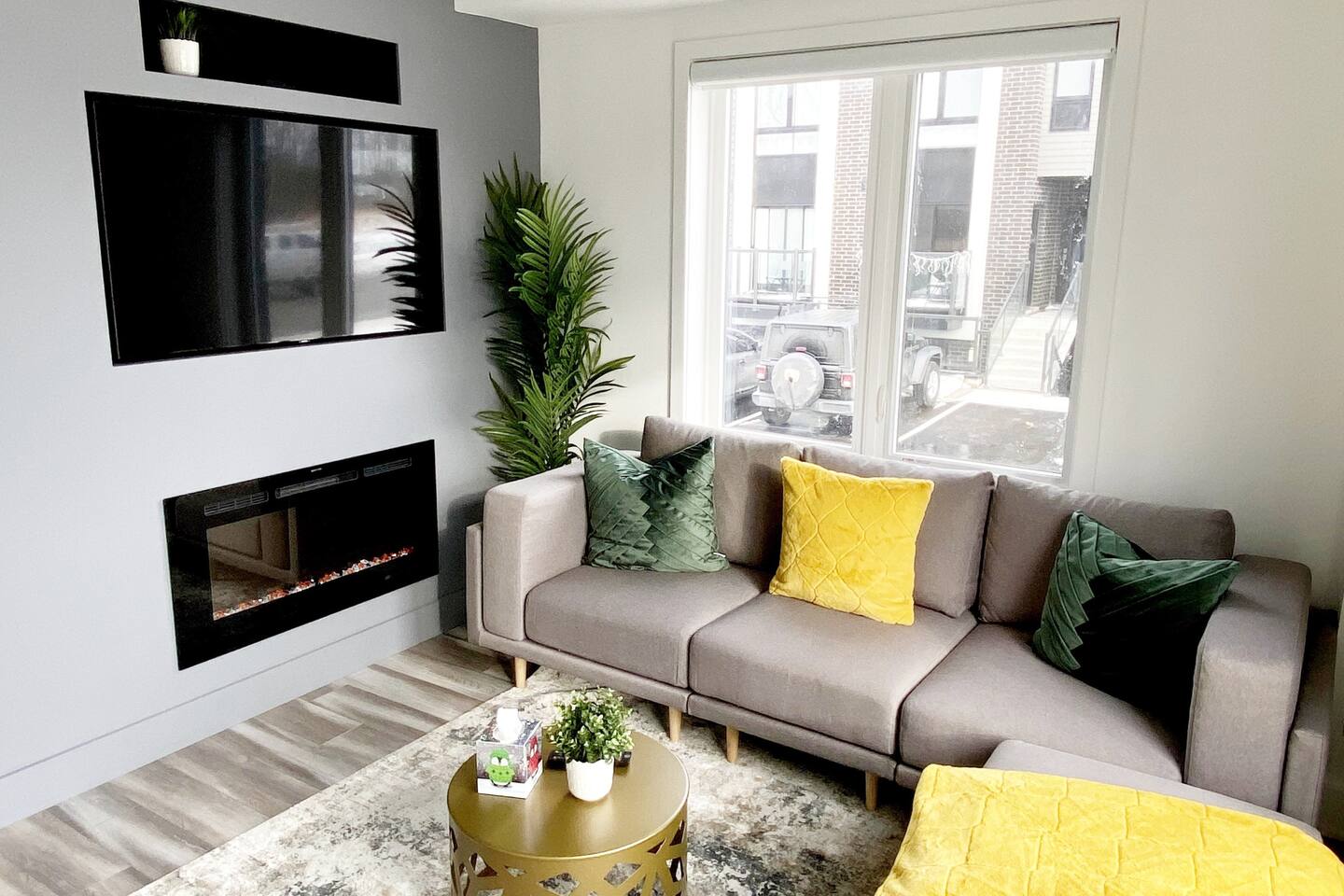 Bright living room with a sofa, fireplace, indoor greenery, and large windows that bring in natural light for a relaxed stay.