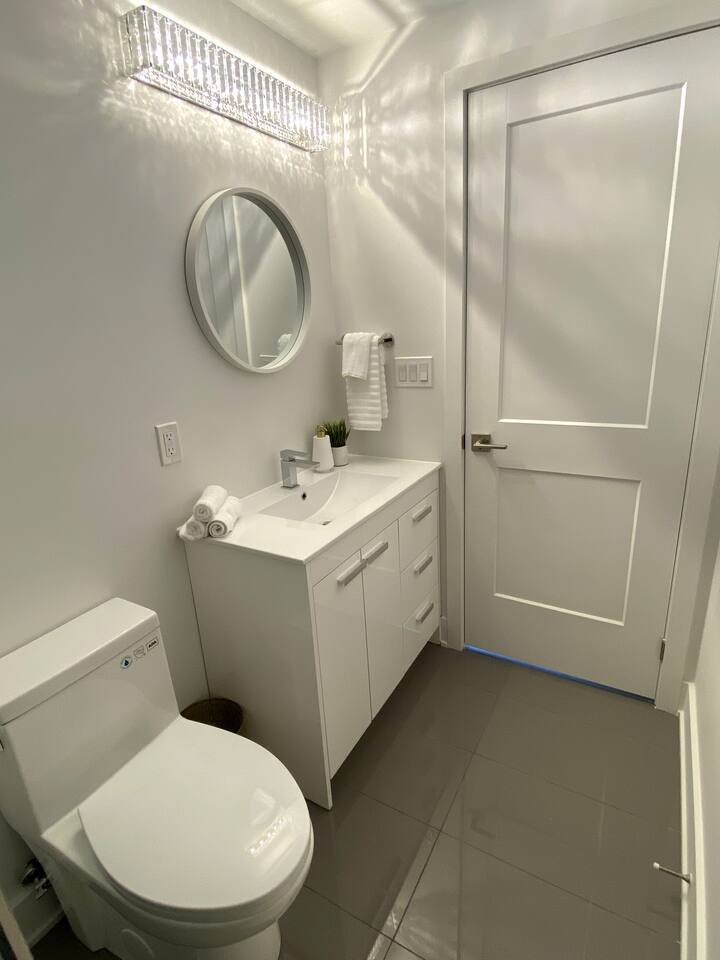 Clean bathroom with a vanity, round mirror, fresh towels, and bright lighting for a simple and comfortable daily routine.