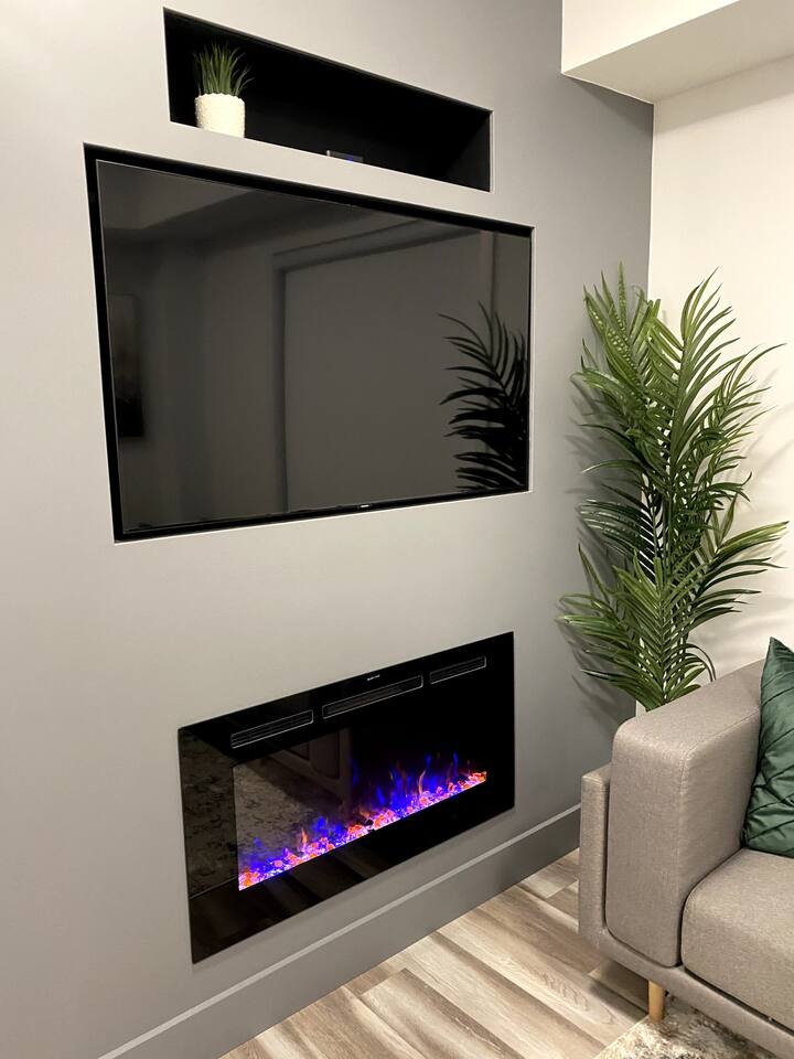 Gas Heated FireplaceWall-mounted TV and electric fireplace create a cozy entertainment area with greenery for a warm, modern feel.