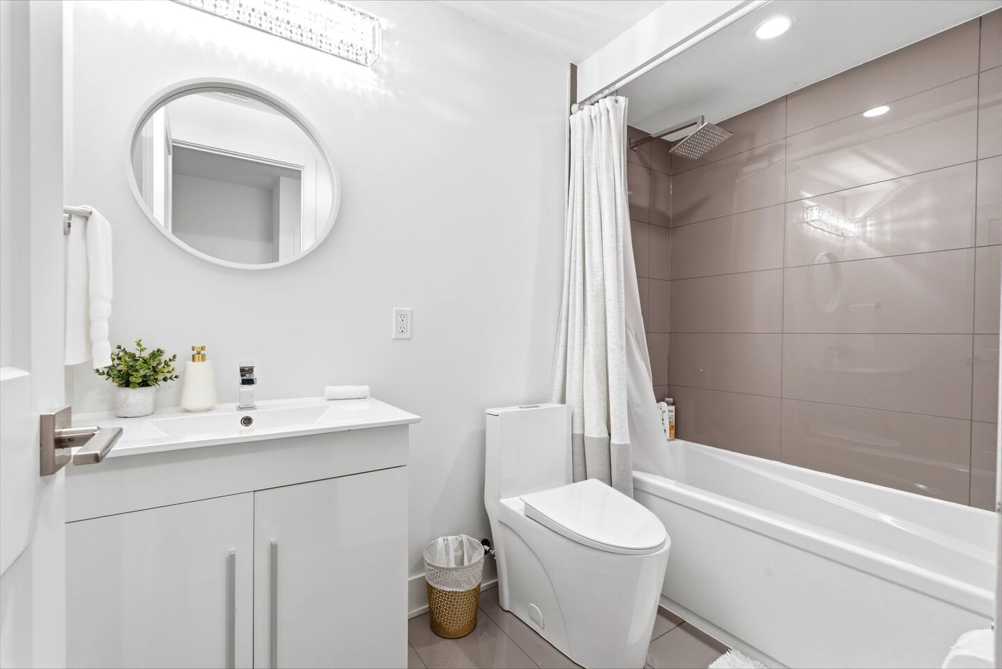 Bright bathroom with a clean vanity, round mirror, and shower-tub combo, offering a fresh and practical space to get ready.