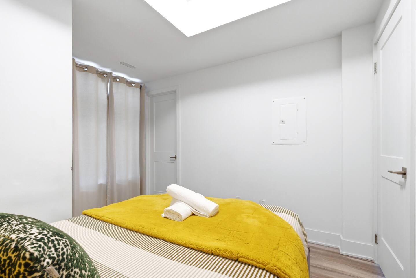 Bright bedroom with soft curtains, fresh towels, and warm yellow bedding, creating a clean and restful space to unwind.