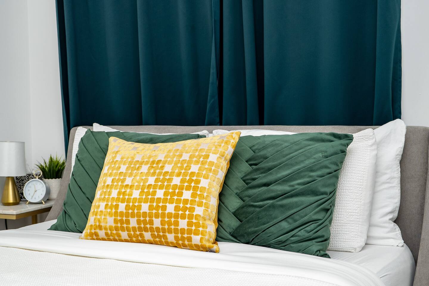 Comfortable bed with layered green and gold pillows, framed by deep curtains for a cozy and restful atmosphere.